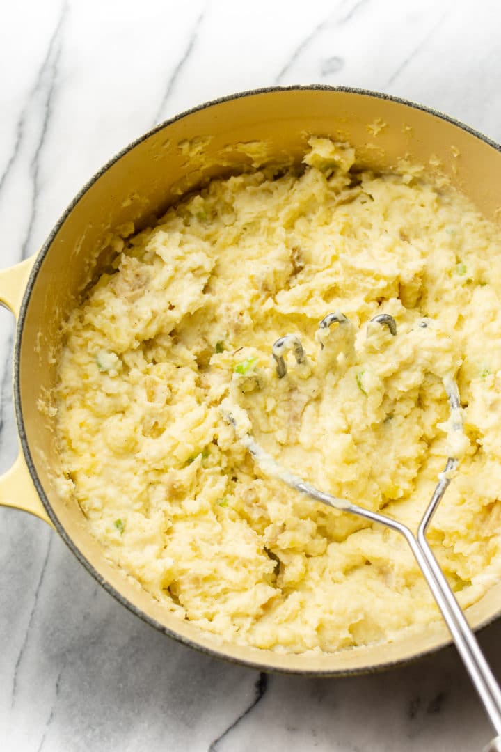 cream cheese mashed potatoes in a yellow pot with potato masher