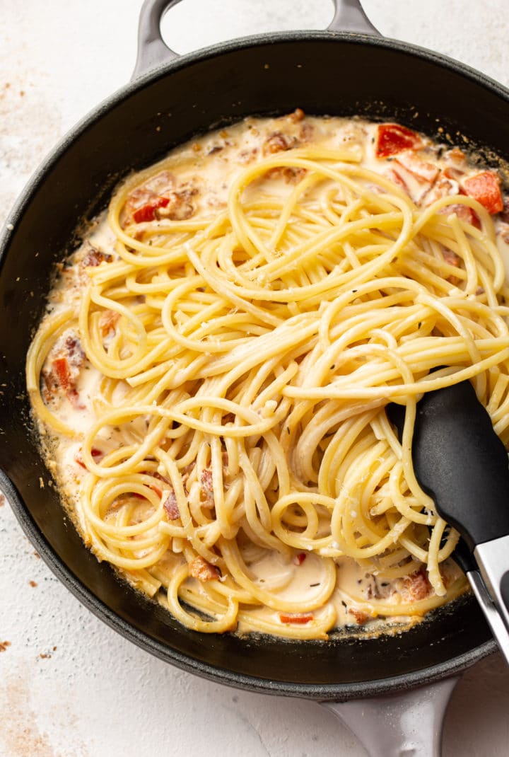 creamy tomato bacon pasta in a skillet with tongs (ready to be tossed)