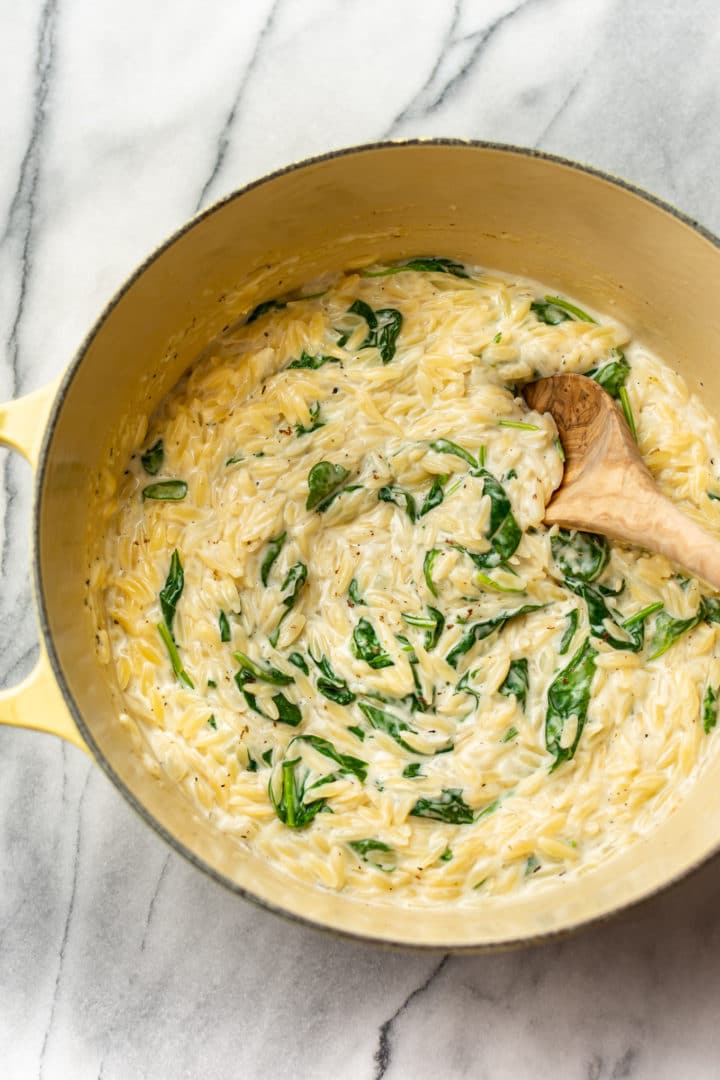 creamy spinach orzo in a pot with a wooden spoon