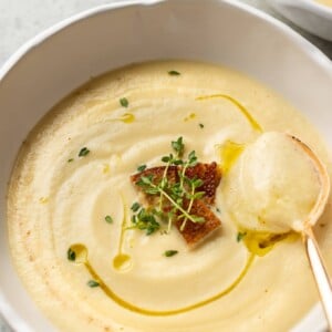 close-up of creamy cauliflower soup in a white bowl with a golden spoon