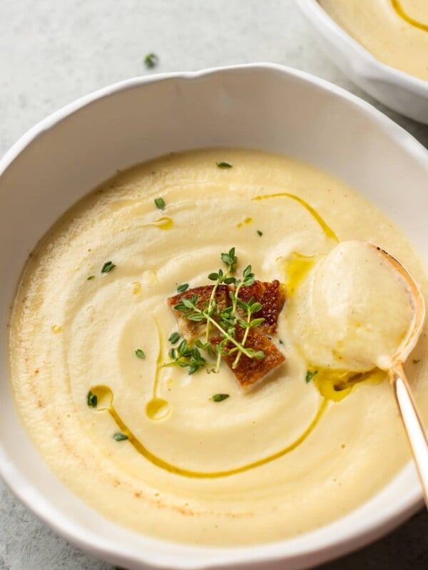 close-up of creamy cauliflower soup in a white bowl with a golden spoon