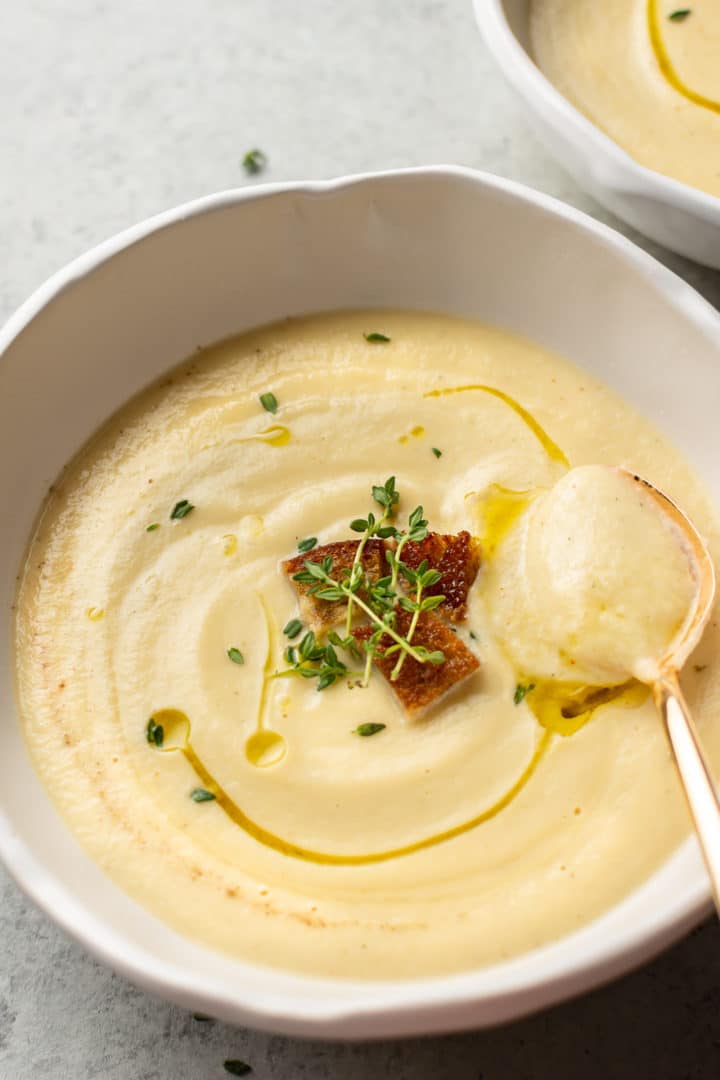 close-up of creamy cauliflower soup in a white bowl with a golden spoon