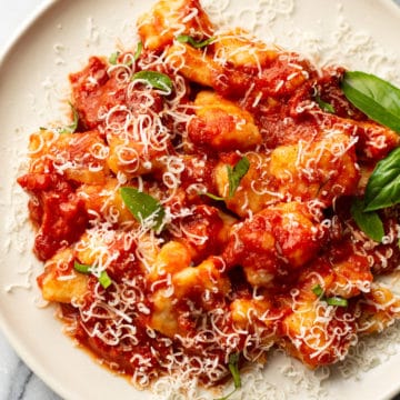 close-up of a plate of homemade gnocchi with marinara sauce (garnished with grated parmesan and fresh basil leaves)
