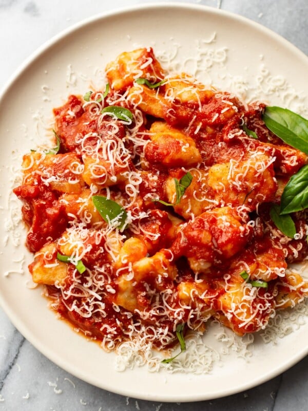 close-up of a plate of homemade gnocchi with marinara sauce (garnished with grated parmesan and fresh basil leaves)