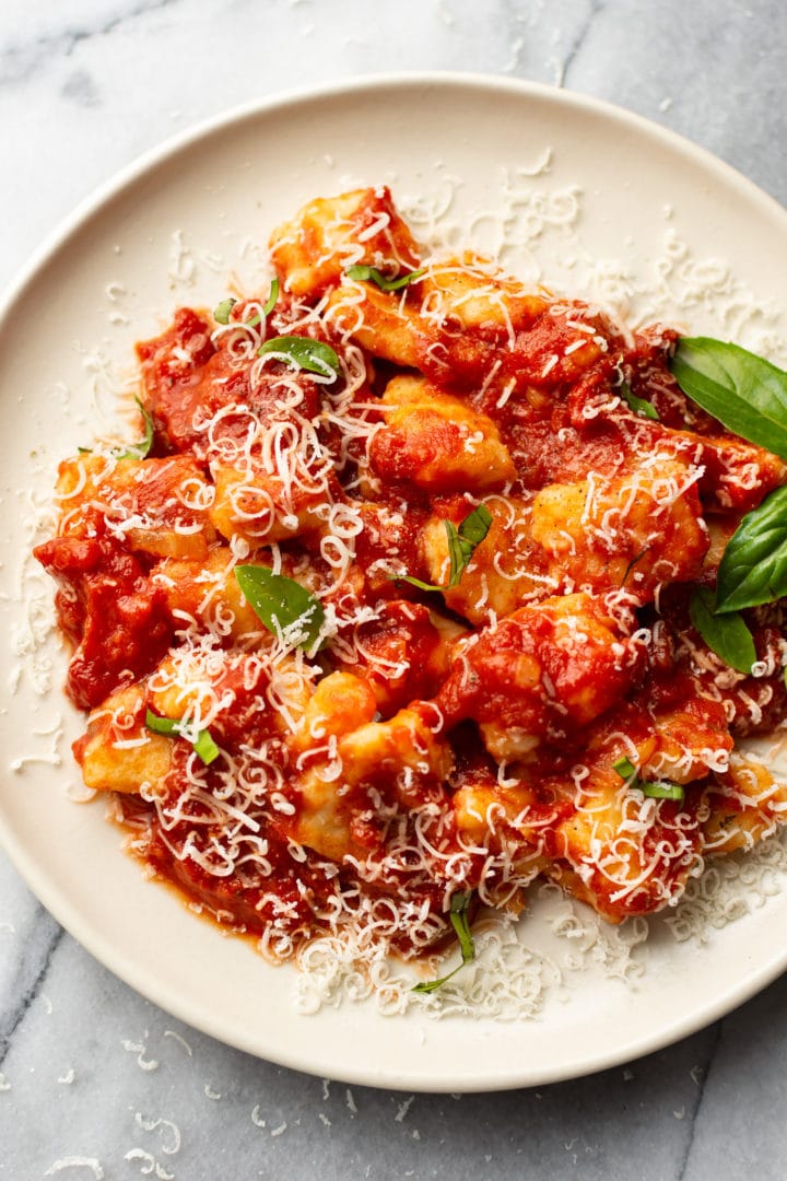 close-up of a plate of homemade gnocchi with marinara sauce (garnished with grated parmesan and fresh basil leaves)