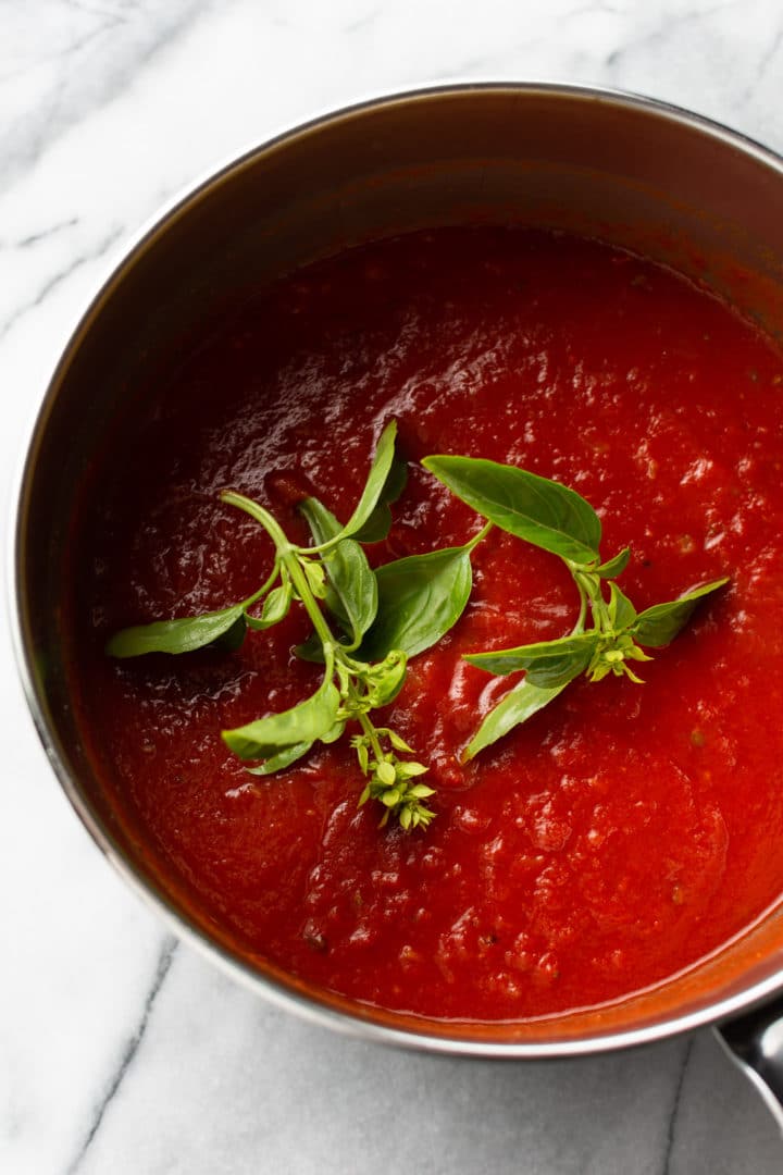 homemade marinara sauce in a pan with fresh basil sprigs on top