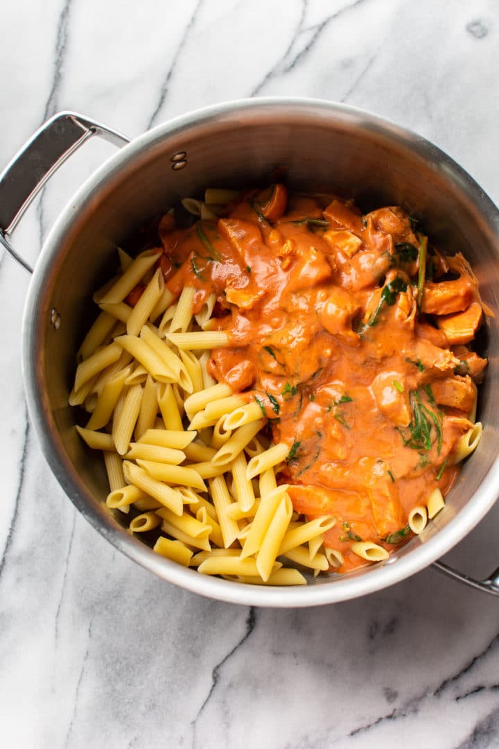 tomato spinach chicken pasta in a pot with cooked penne (ready to be tossed with pasta)