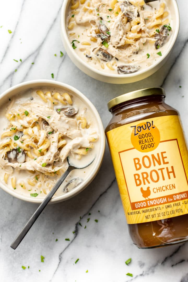Chicken Tetrazzini Soup in two bowls with a jar of Zoup! Chicken Bone Broth
