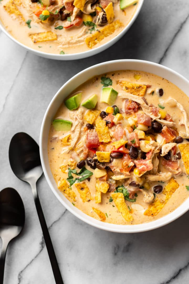 easy chicken taco soup in two white bowls (with spoons on the marble background)