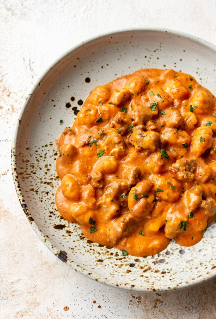 close-up of cheesy gnocchi with bratwurst sausage in a shallow bowl