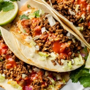 ground beef taco recipe (the best ground beef tacos loaded with toppings on a white plate)