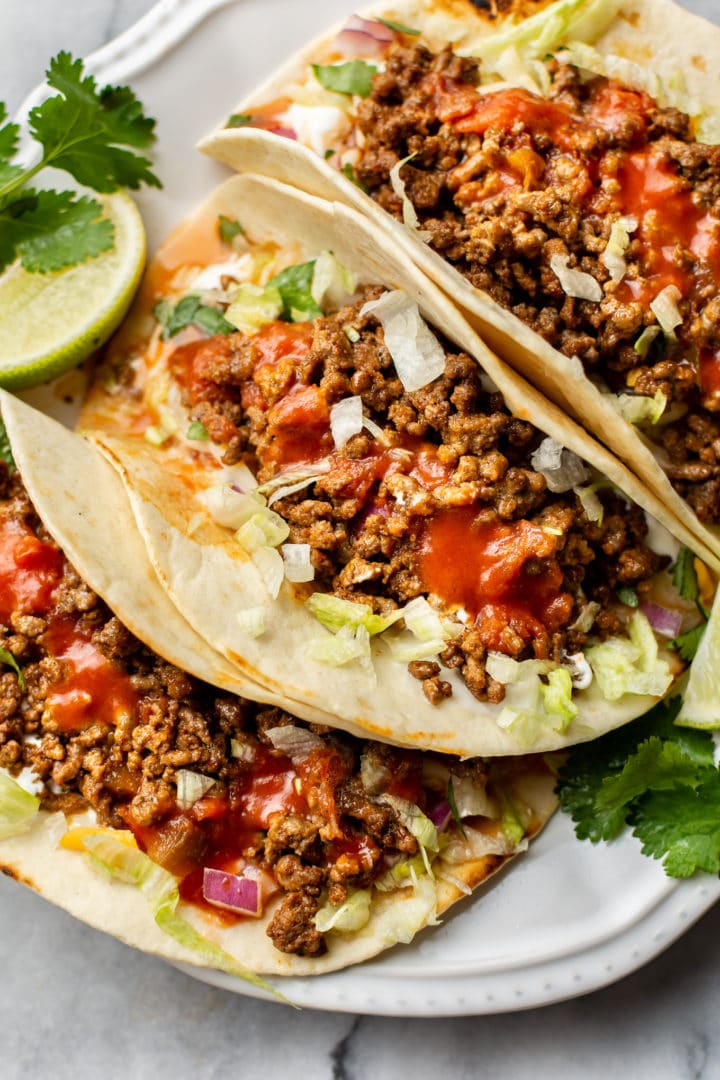 ground beef taco recipe (the best ground beef tacos loaded with toppings on a white plate)