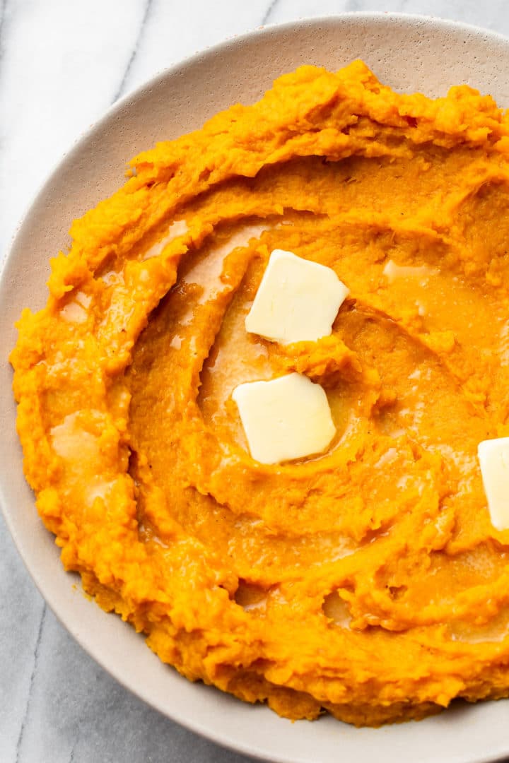 close-up of mashed butternut squash in a serving bowl with pats of butter