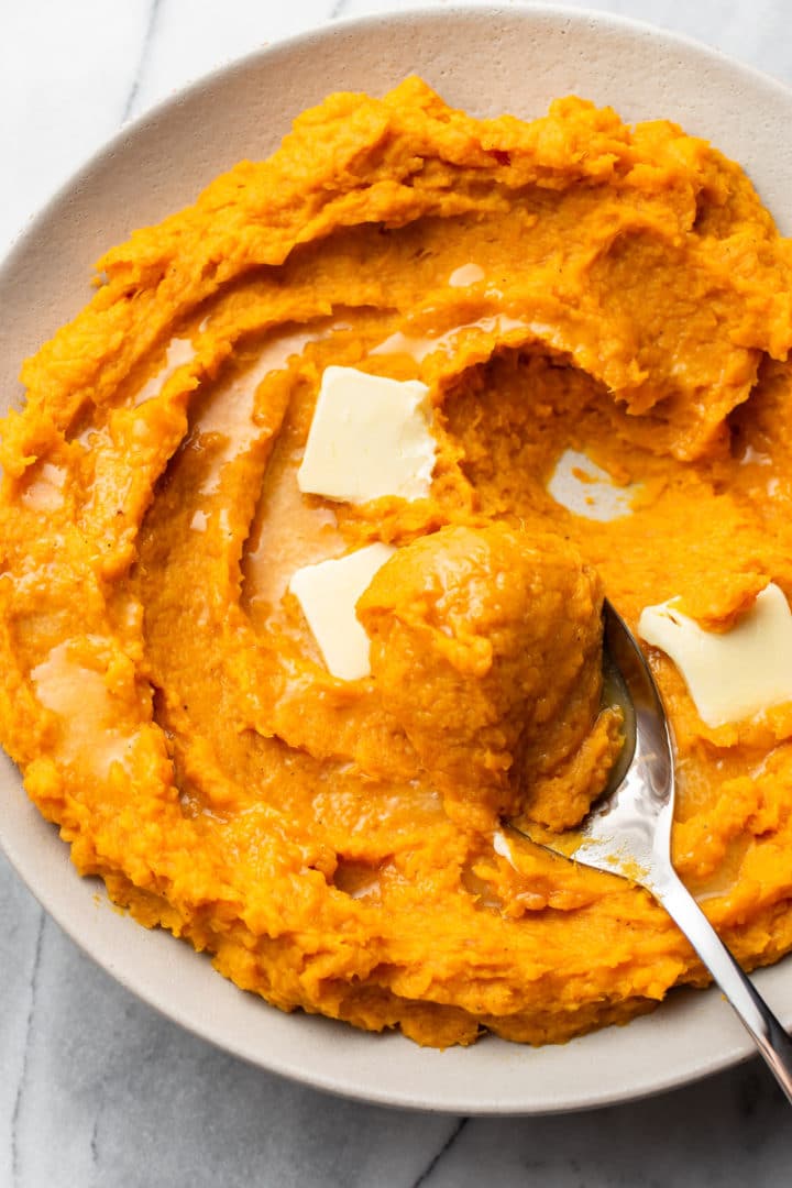 mashed butternut squash in a serving bowl with a spoonful being lifted out
