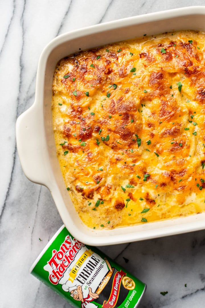 Cajun scalloped potatoes in a baking dish with a container of Tony Chachere's Creole Seasoning