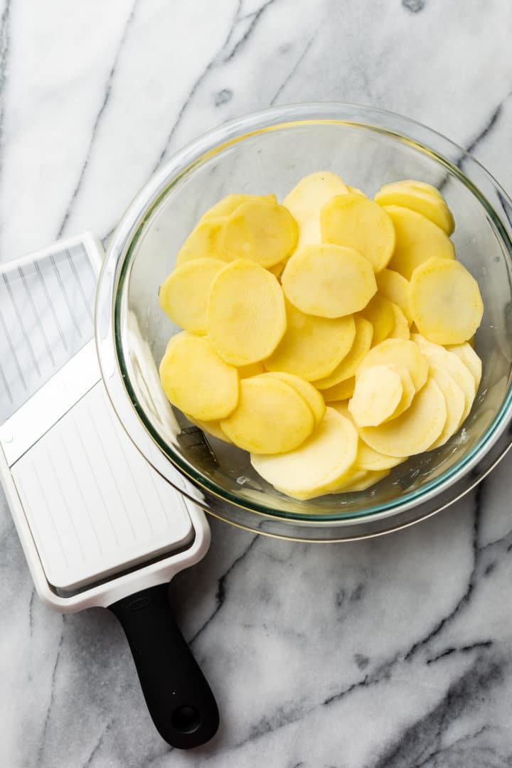 mandoline slicer and sliced potatoes in a glass bowl