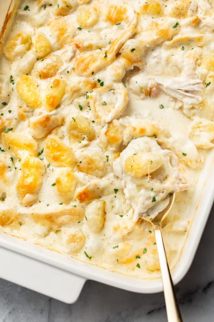 close-up of chicken Alfredo baked gnocchi in a baking dish with a serving spoonful being lifted out