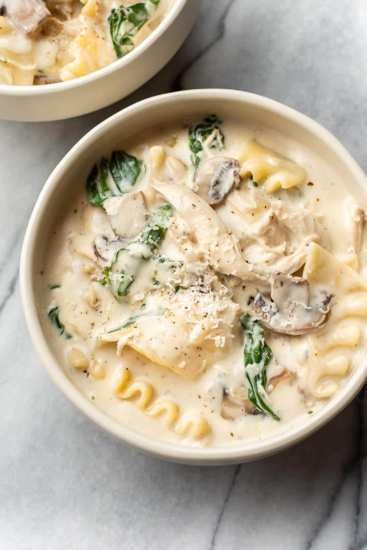 creamy white chicken lasagna soup in two bowls on a marble background