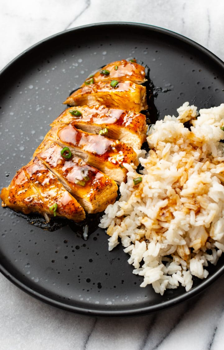 sliced honey garlic chicken breast on a plate with rice and sauce