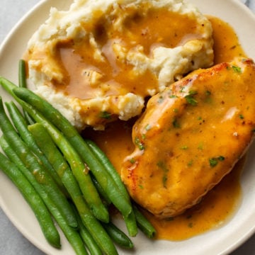 chicken and gravy with mashed potatoes and green beans on a plate