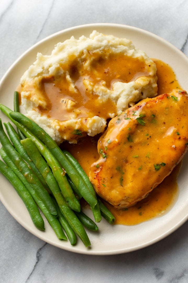 chicken and gravy with mashed potatoes and green beans on a plate