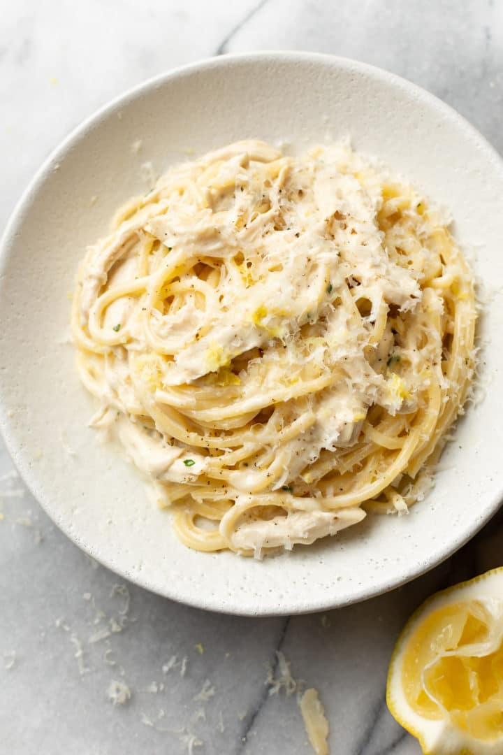 creamy lemon chicken pasta in a shallow bowl with a lemon wedge beside it