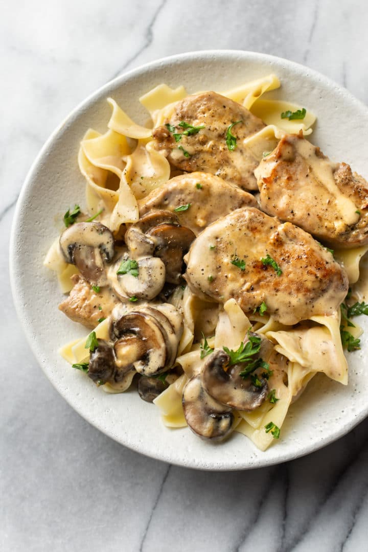 pork tenderloin with creamy mushroom sauce over egg noodles in a shallow bowl