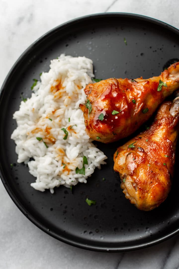honey baked drumsticks on a black plate with rice