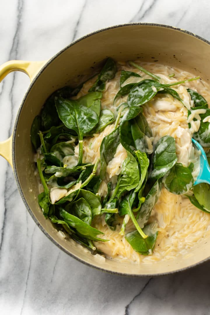 lemon chicken orzo in a yellow pot (fresh spinach is being added in)