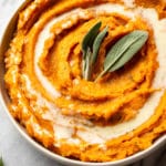 rosemary and sage mashed sweet potatoes in a serving bowl, garnished with fresh sage