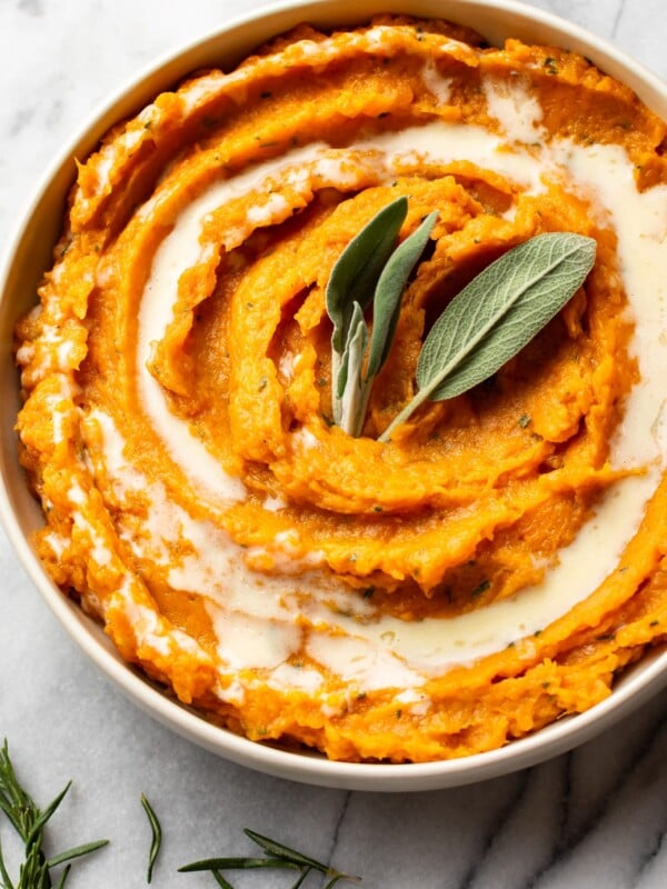 rosemary and sage mashed sweet potatoes in a serving bowl, garnished with fresh sage