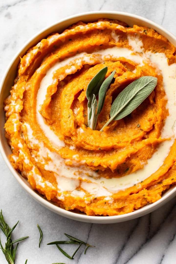 rosemary and sage mashed sweet potatoes in a serving bowl, garnished with fresh sage