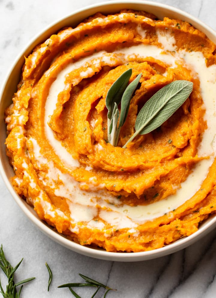 rosemary and sage mashed sweet potatoes in a serving bowl, garnished with fresh sage