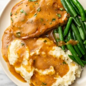 a plate with a ranch pork chop, mashed potatoes, and green beans