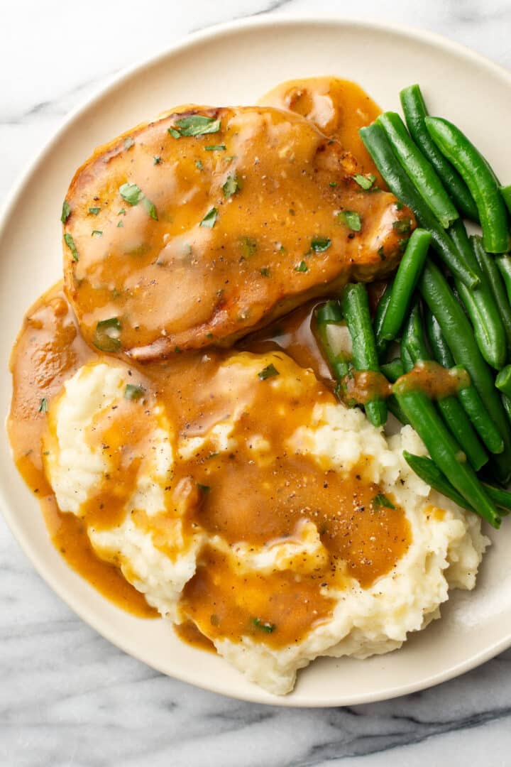 a plate with a ranch pork chop, mashed potatoes, and green beans