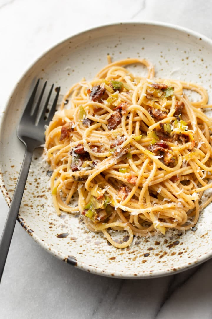 bacon leek pasta in a shallow bowl with a fork on the side