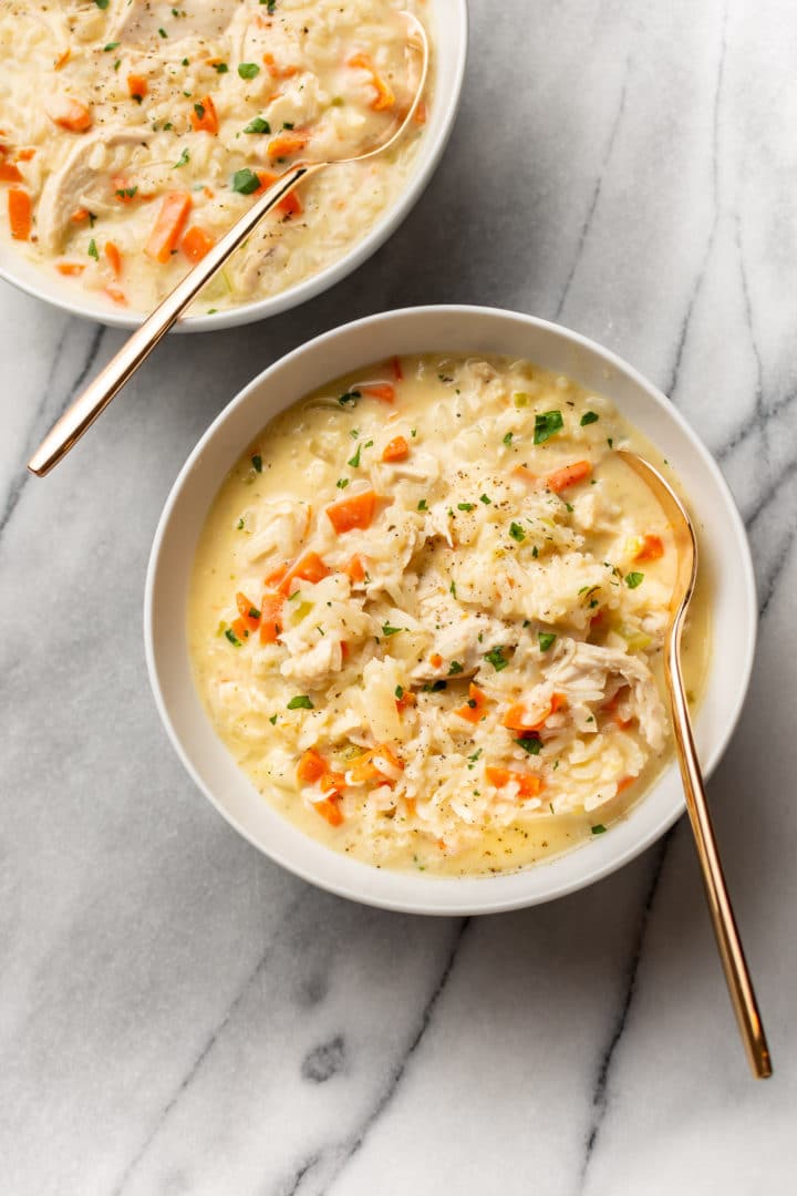 cream of chicken and rice soup in two white bowls with gold spoons