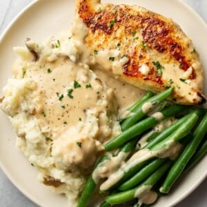 creamy garlic parmesan chicken on a plate with mashed potatoes, green beans, and plenty of sauce