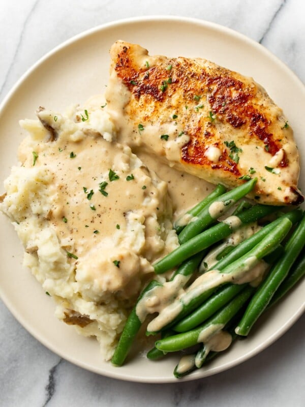 creamy garlic parmesan chicken on a plate with mashed potatoes, green beans, and plenty of sauce