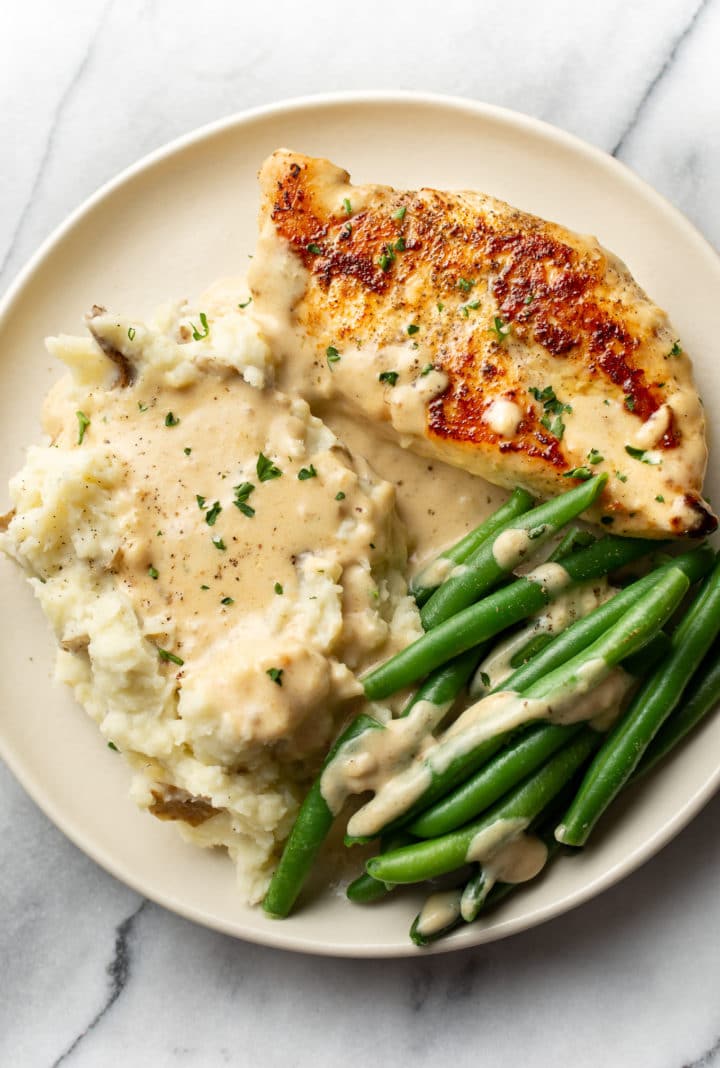 creamy garlic parmesan chicken on a plate with mashed potatoes, green beans, and plenty of sauce