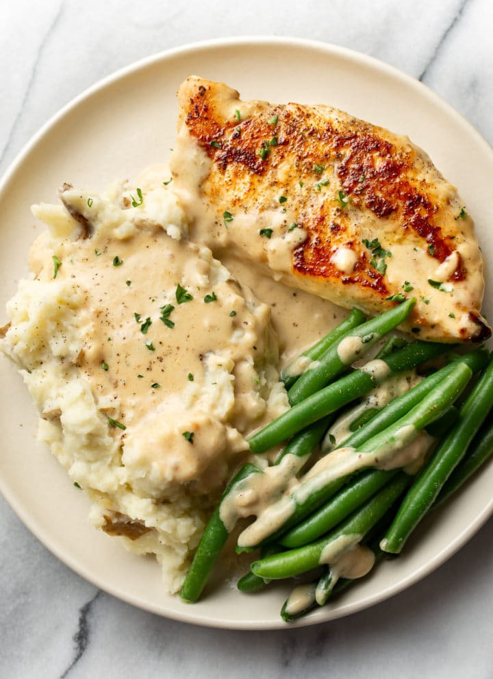 creamy garlic parmesan chicken on a plate with mashed potatoes, green beans, and plenty of sauce