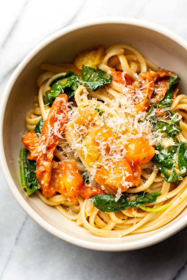 close-up of garlic butter pasta with fresh tomatoes and spinach in a bowl