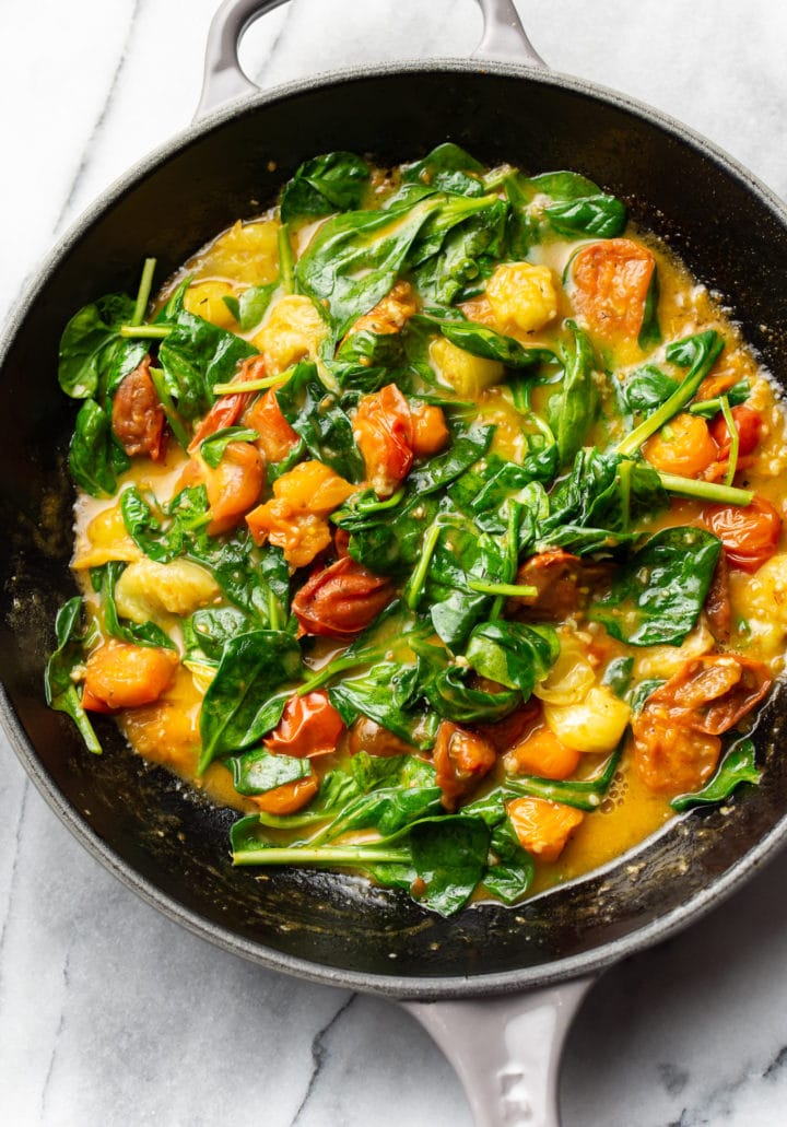 garlic butter pasta sauce with spinach and fresh tomatoes in a skillet