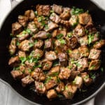 garlic steak bites with parsley sprinkled on top in a skillet