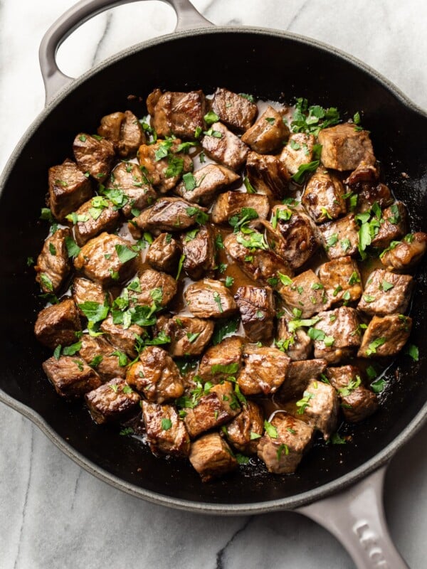 garlic steak bites with parsley sprinkled on top in a skillet