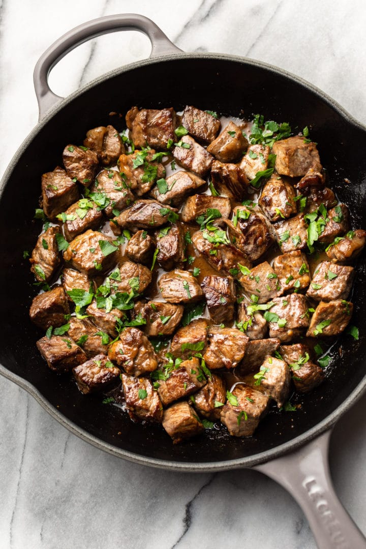 garlic steak bites with parsley sprinkled on top in a skillet