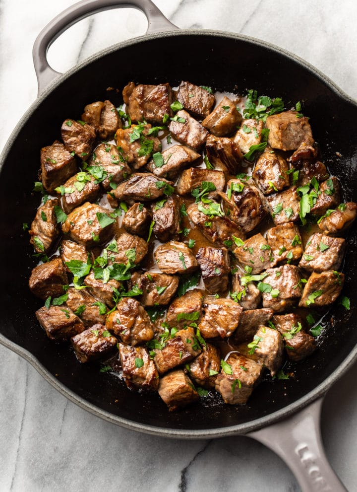 garlic steak bites with parsley sprinkled on top in a skillet