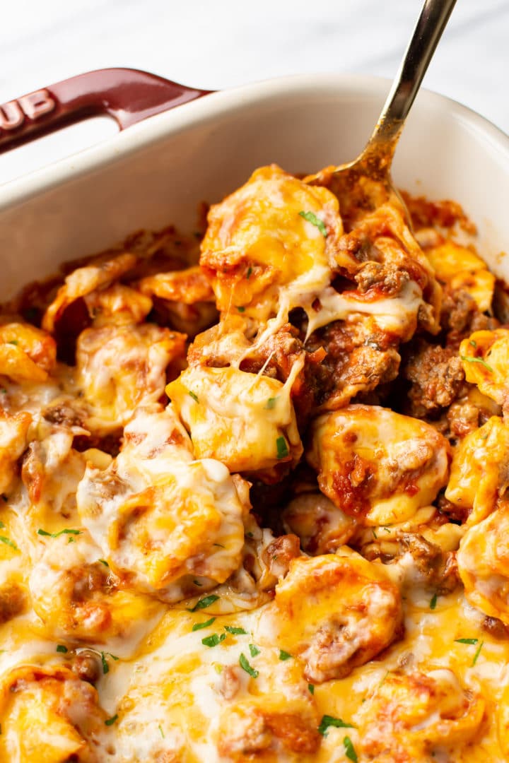 close-up of a spoonful of cheesy baked tortellini in a Staub baking dish