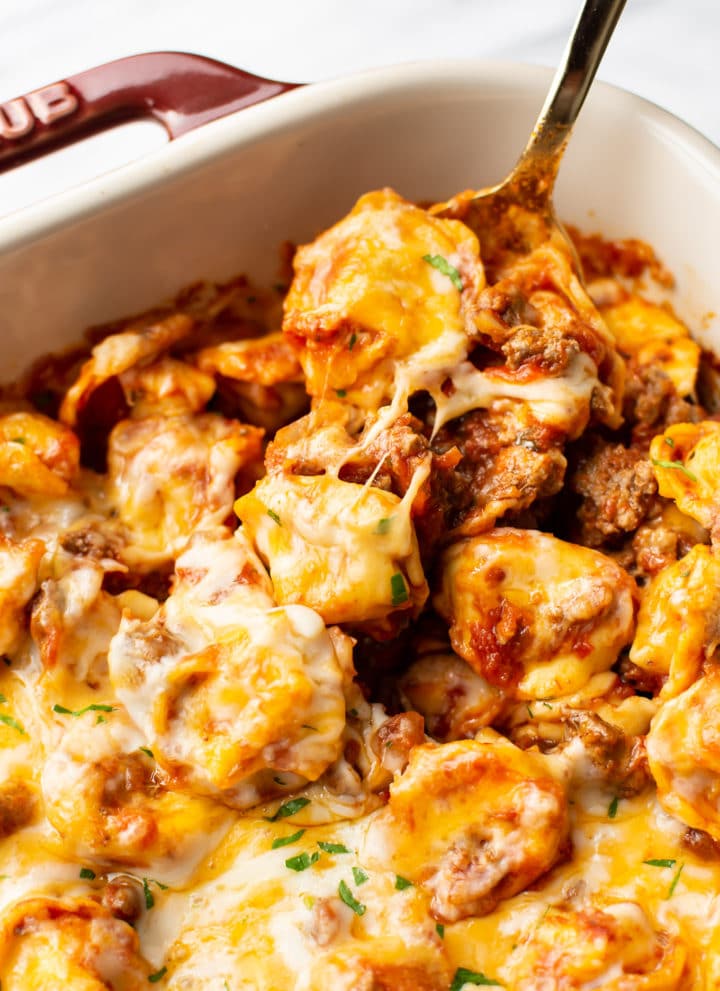 close-up of a spoonful of cheesy baked tortellini in a Staub baking dish