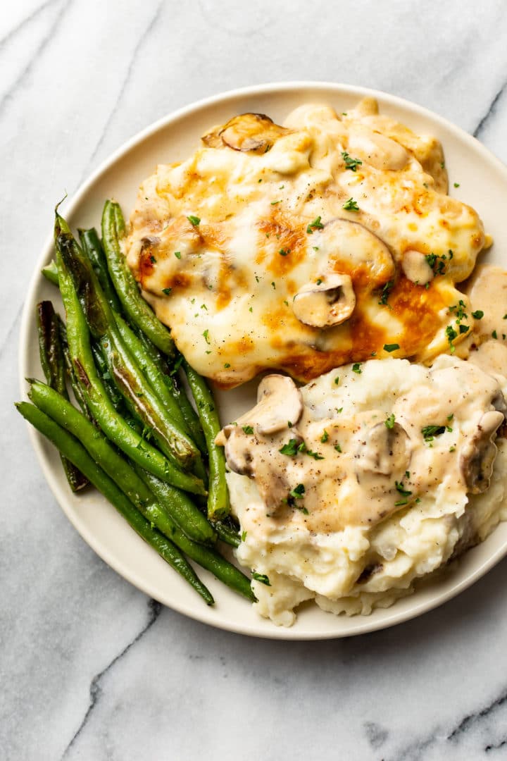 Chicken Gloria plated with mashed potatoes, roasted green beans, and plenty of creamy mushroom sherry sauce